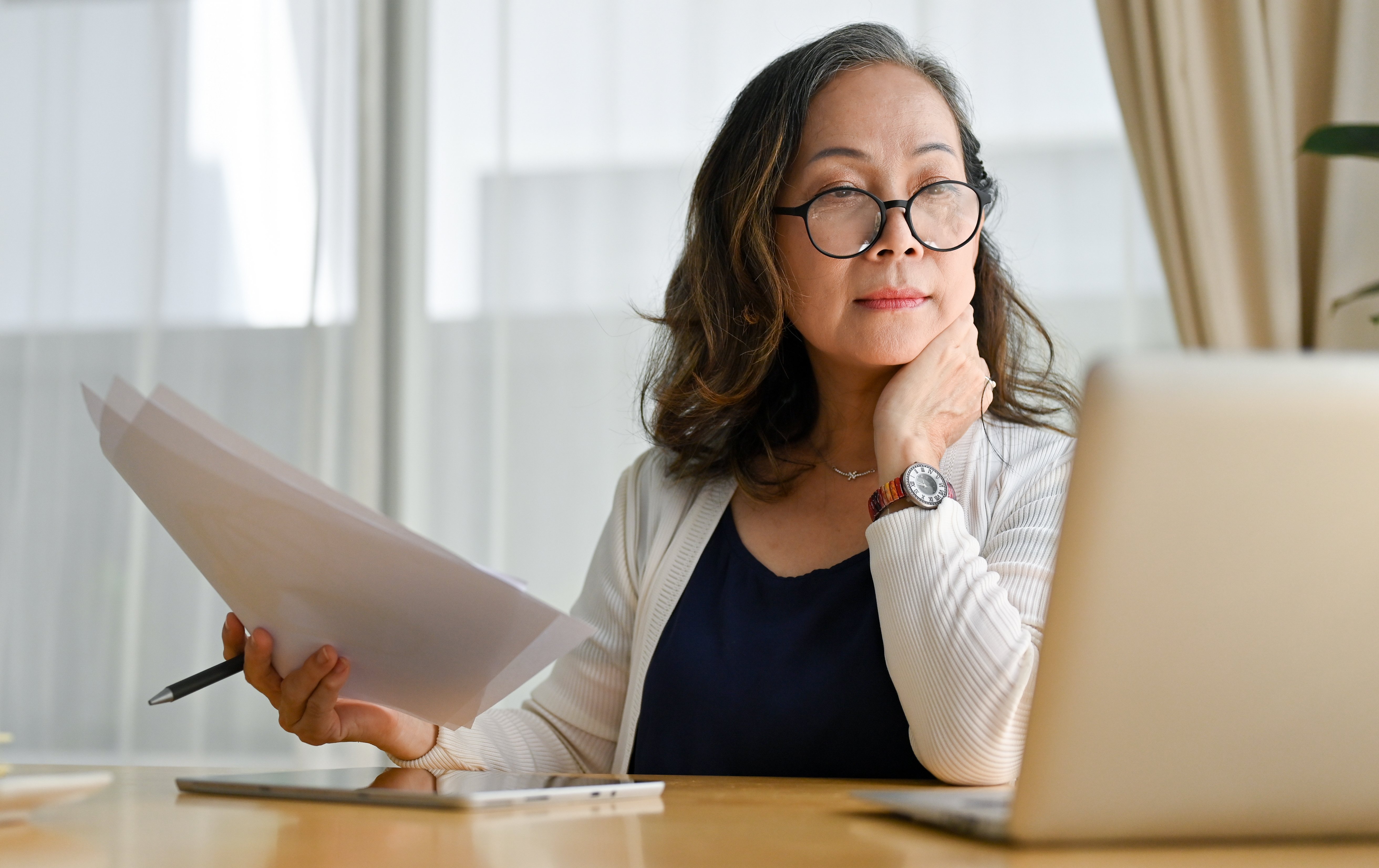 Eine Frau sitzt konzentriert vor ihrem Laptop und hält ein Blatt Papier in der Hand