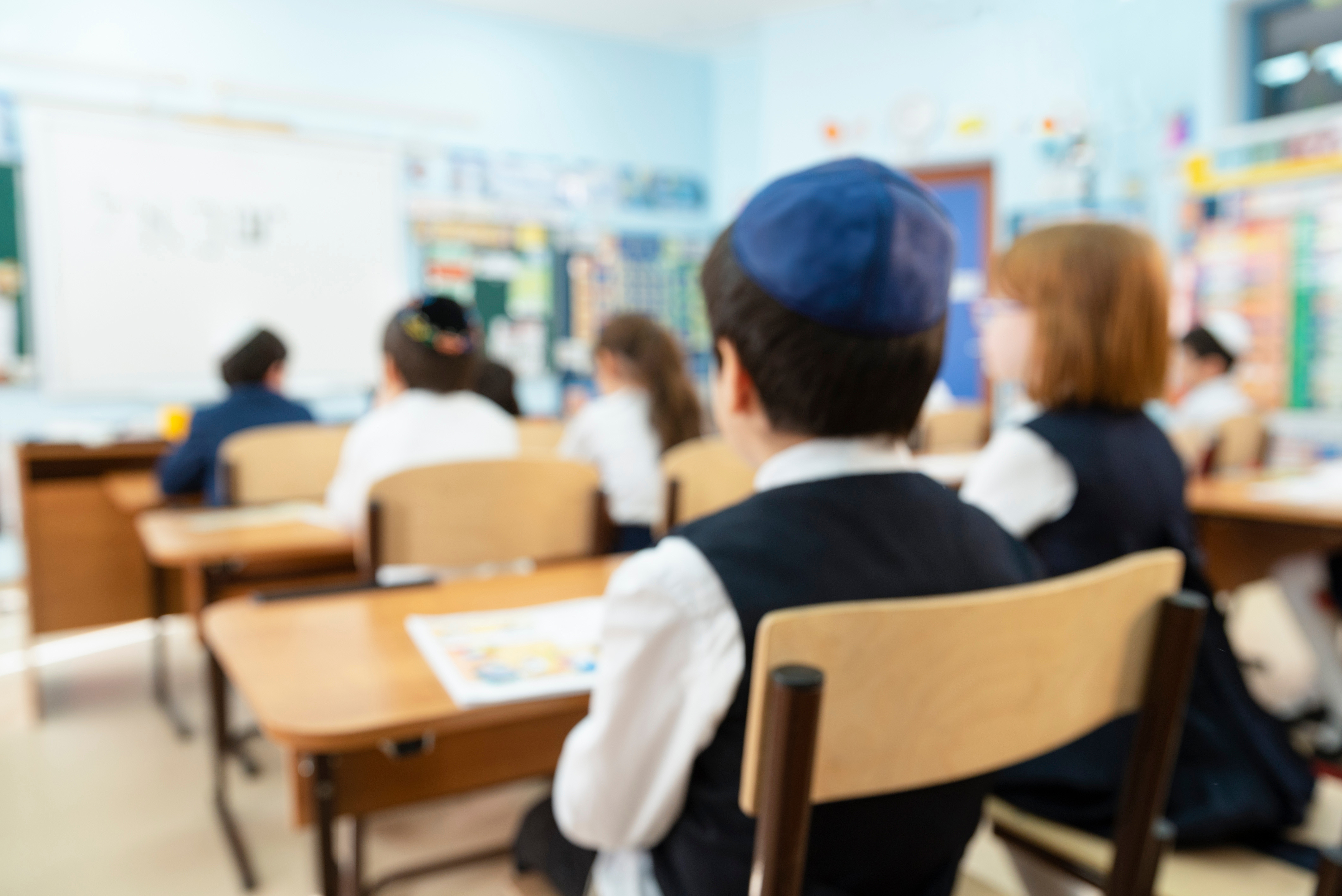 Jüdischer Junge sitzt an seinem Tisch in der Schule, mit dem Rücken zur Kamera. Er trägt eine Kippa.