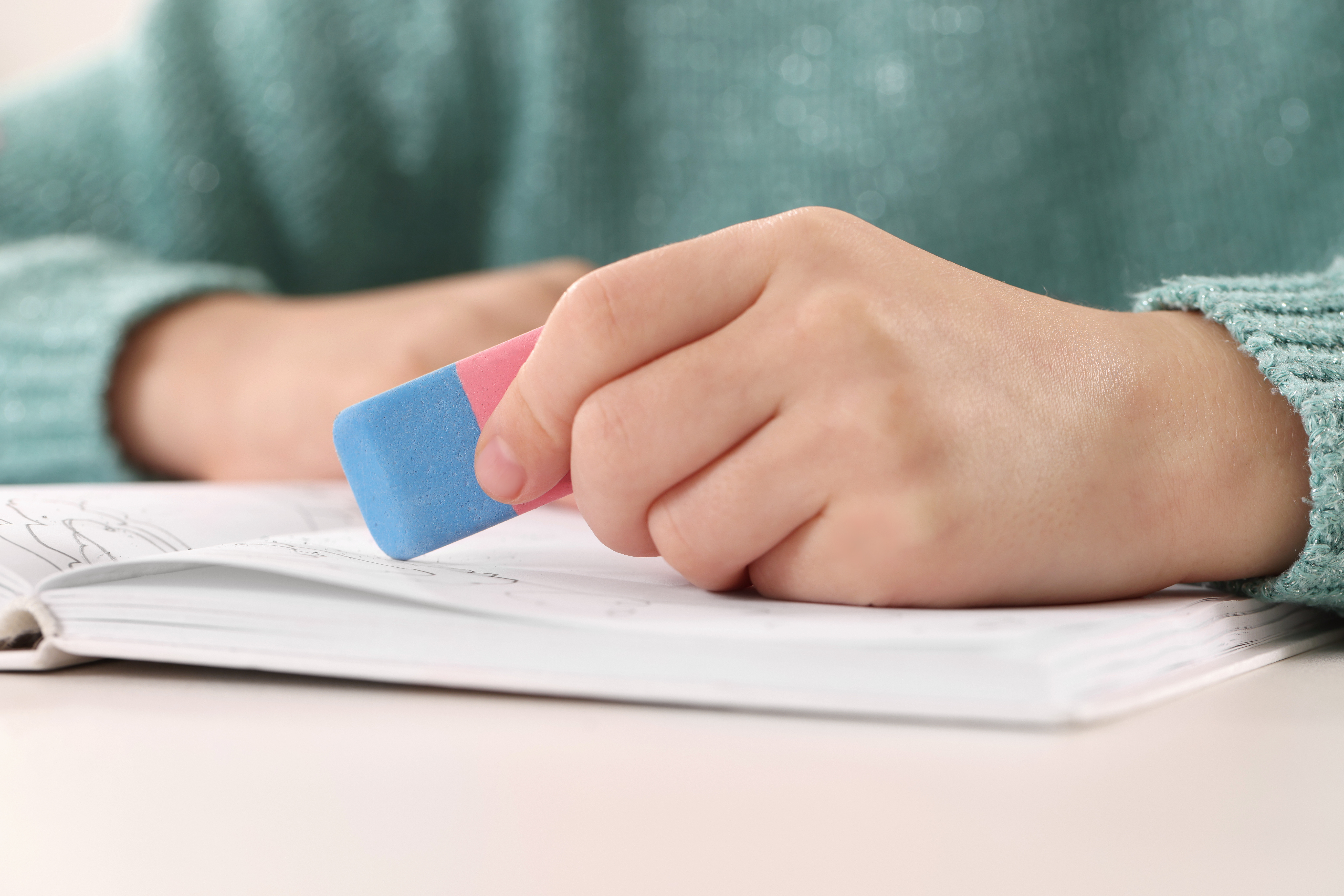 Kind hält rot-blauen Radiergummi in der Hand und radiert im Heft.