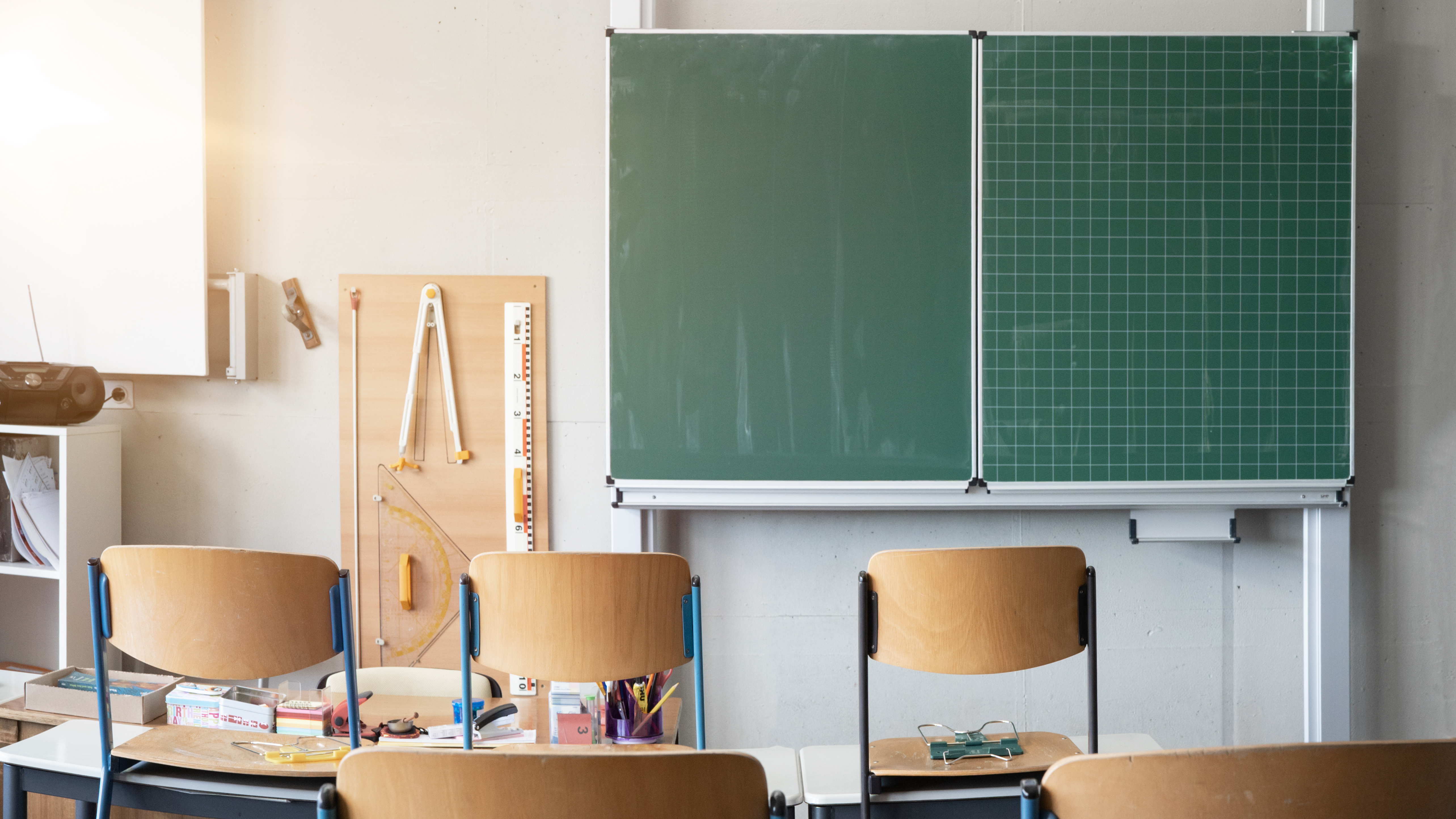 Leeres Klassenzimmer, Blick auf leere Tafel, aufgestuhlte Holzstühle, Geodreieck an der Wand